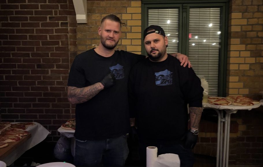 Zwei Männer in schwarzen T-Shirts stehen zusammen, lächeln und posieren.