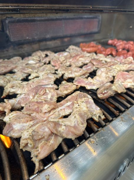 Gegrilltes Fleisch, darunter Hähnchen und Würstchen, auf einem Grill.